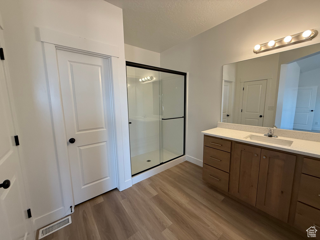 Bathroom featuring a stall shower, wood finished floors, vanity, a textured ceiling, and baseboards