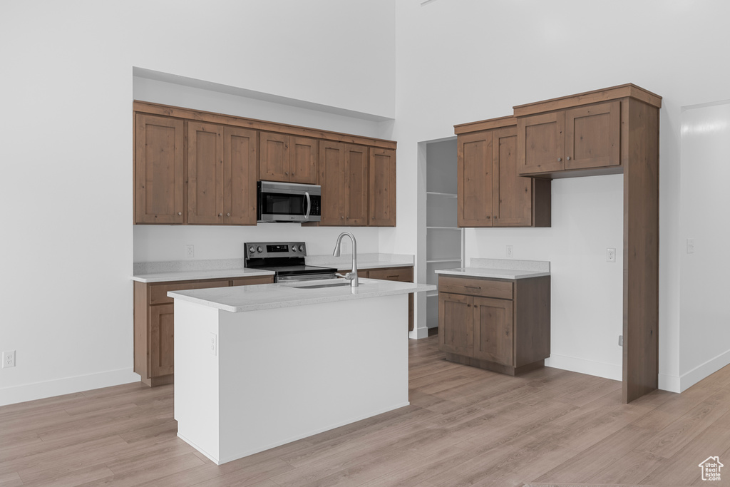 Kitchen with stainless steel appliances, light wood-style floors, light countertops, a high ceiling, and a center island with sink