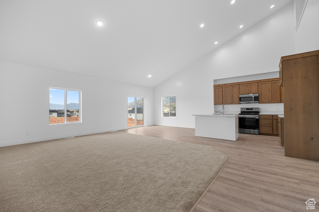Unfurnished living room with high vaulted ceiling, recessed lighting, and light wood finished floors