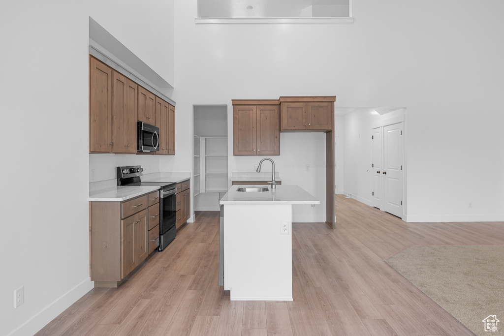 Kitchen featuring stainless steel appliances, a high ceiling, light countertops, light wood-style floors, and brown cabinets