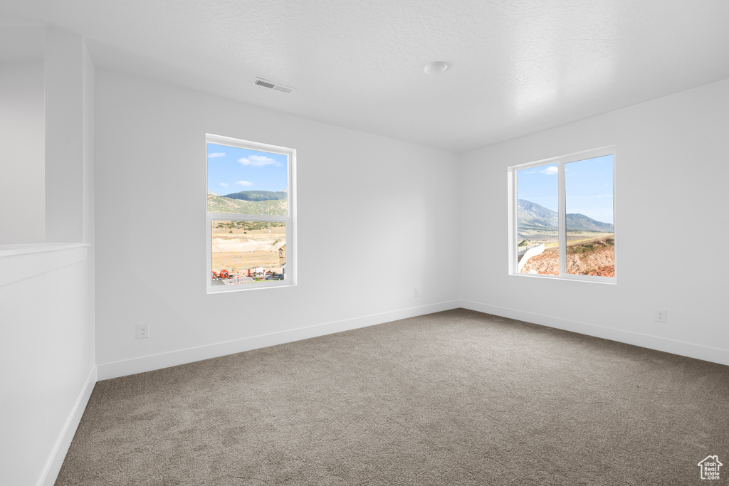Carpeted empty room featuring healthy amount of natural light and a mountain view