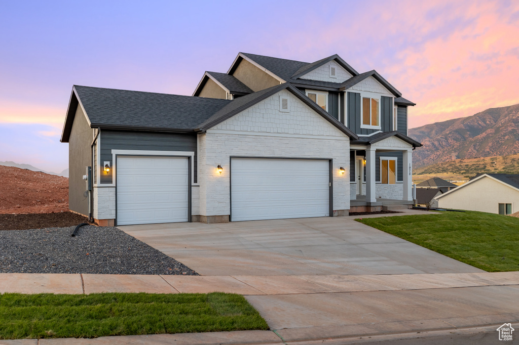 View of front of home featuring an attached garage, driveway, a mountain view, roof with shingles, and a front yard
