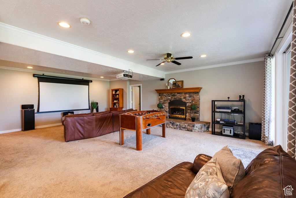 Cinema room with carpet floors, a stone fireplace, crown molding, ceiling fan, and a textured ceiling
