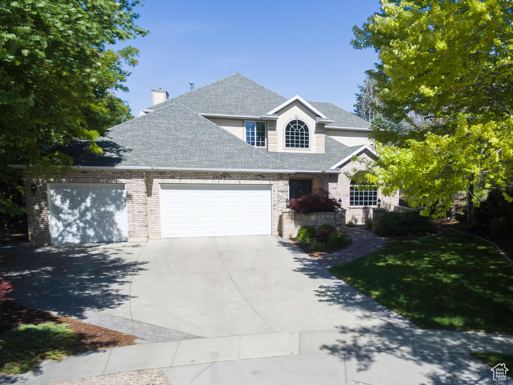 Traditional-style home featuring concrete driveway, an attached garage, roof with shingles, brick siding, and a chimney