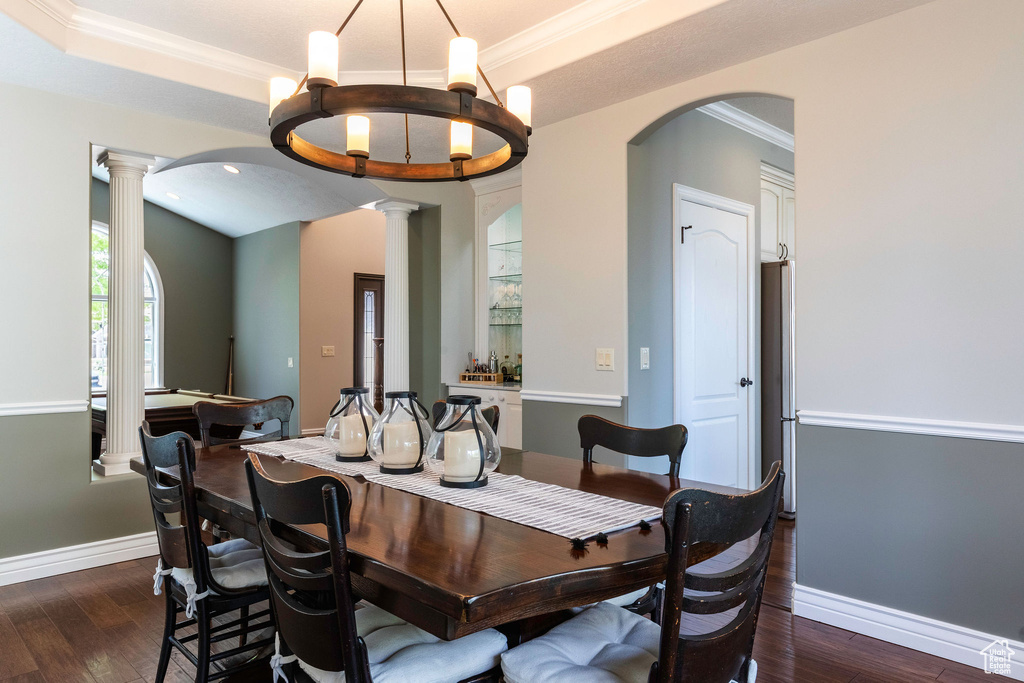 Dining area with dark wood-style flooring, arched walkways, ornate columns, a chandelier, and ornamental molding