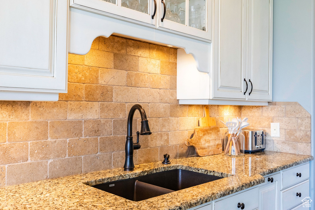 Kitchen featuring glass insert cabinets, white cabinetry, backsplash, and light stone countertops