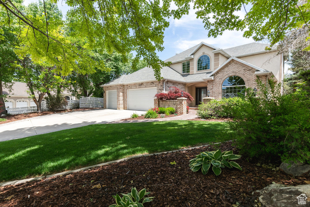 Traditional-style house with a garage, concrete driveway, a front yard, brick siding, and roof with shingles