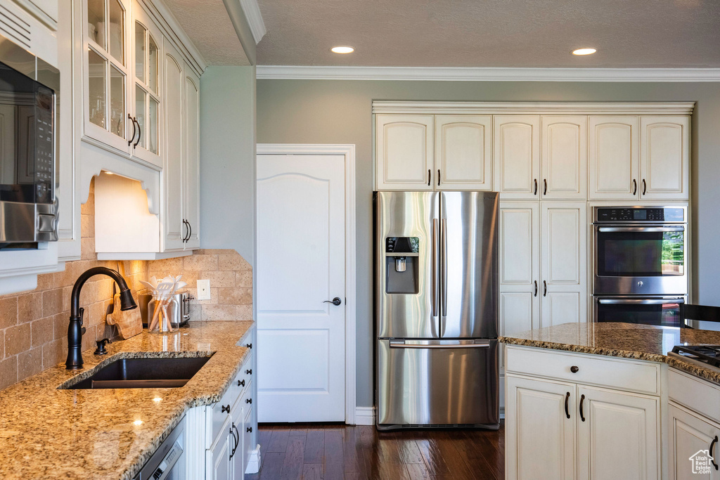Kitchen featuring stainless steel appliances, crown molding, dark wood-style flooring, cream cabinets, and light stone counters