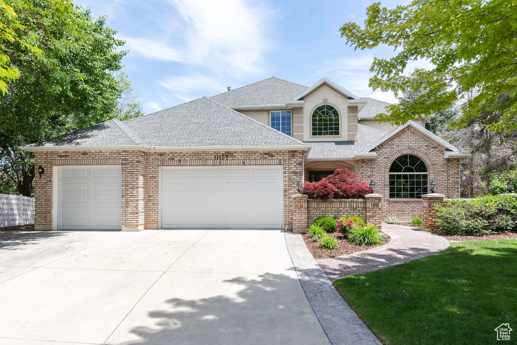 Traditional-style house featuring an attached garage, driveway, stucco siding, roof with shingles, and brick siding