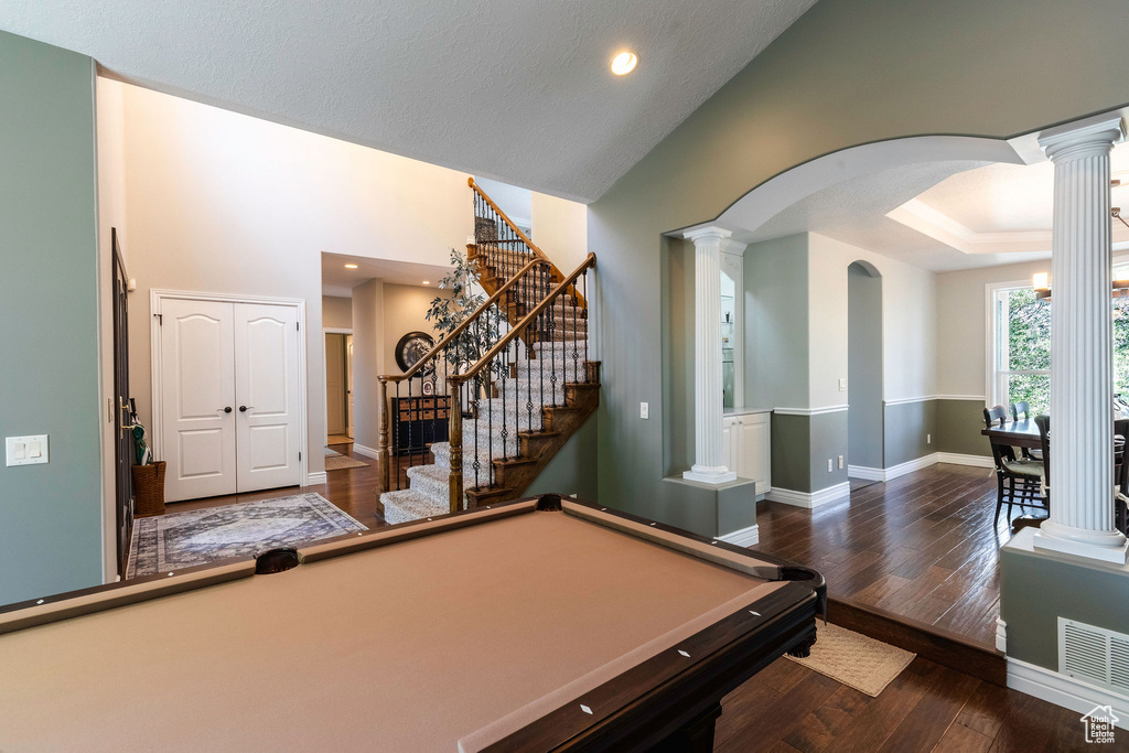 Recreation room with arched walkways, ornate columns, billiards table, wood finished floors, and high vaulted ceiling