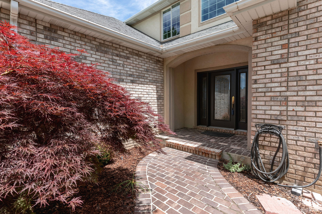 View of exterior entry with brick siding and a shingled roof