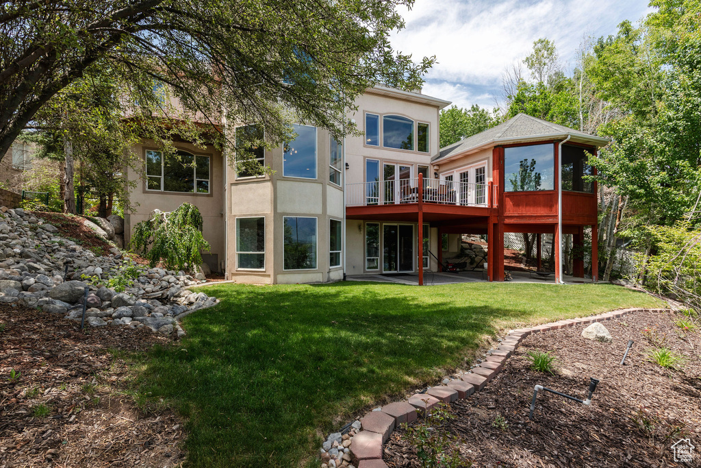 Back of house with a patio area, a lawn, a deck, a sunroom, and stucco siding