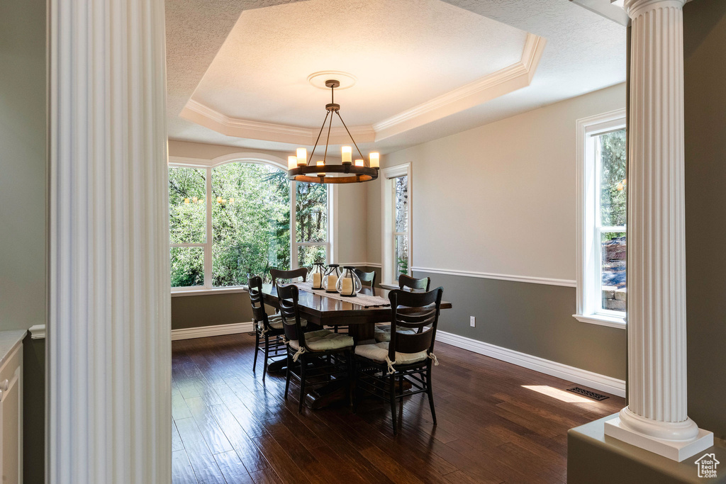 Dining area featuring decorative columns, a tray ceiling, dark wood-type flooring, crown molding, and a chandelier