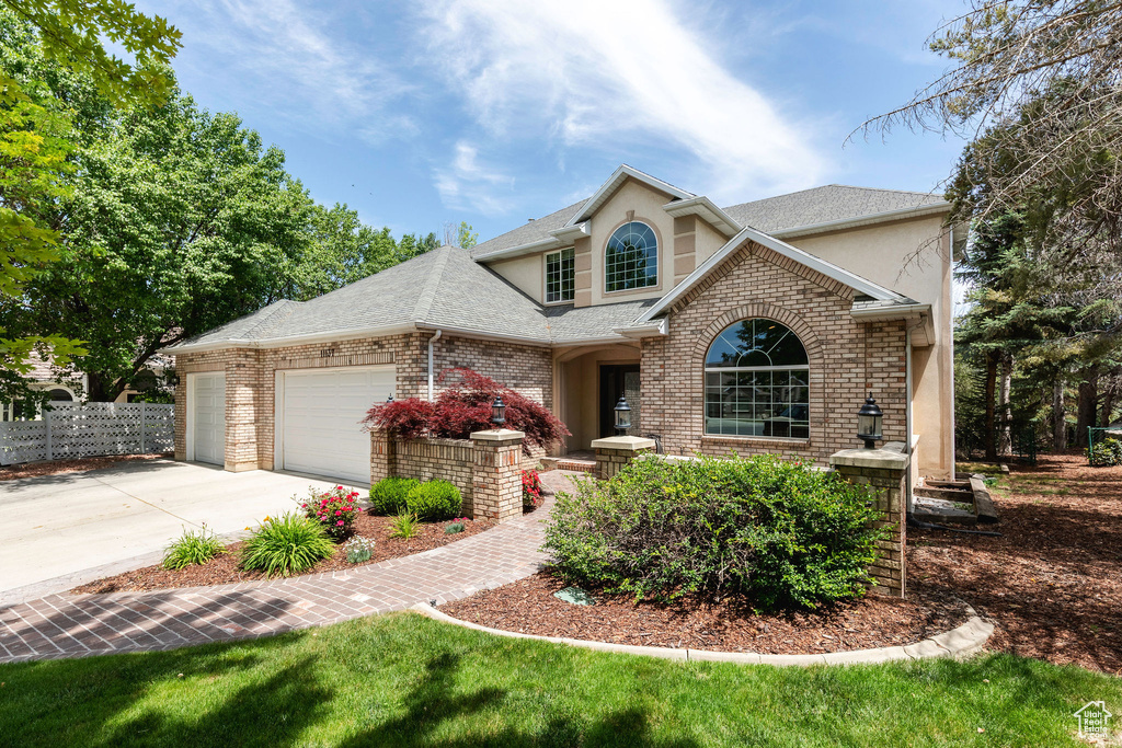 Traditional home with stucco siding, a garage, driveway, and roof with shingles
