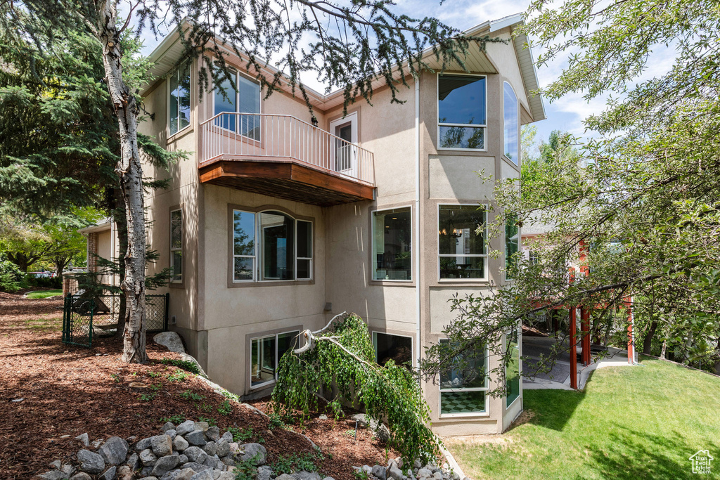 Back of property featuring a balcony, stucco siding, and a yard