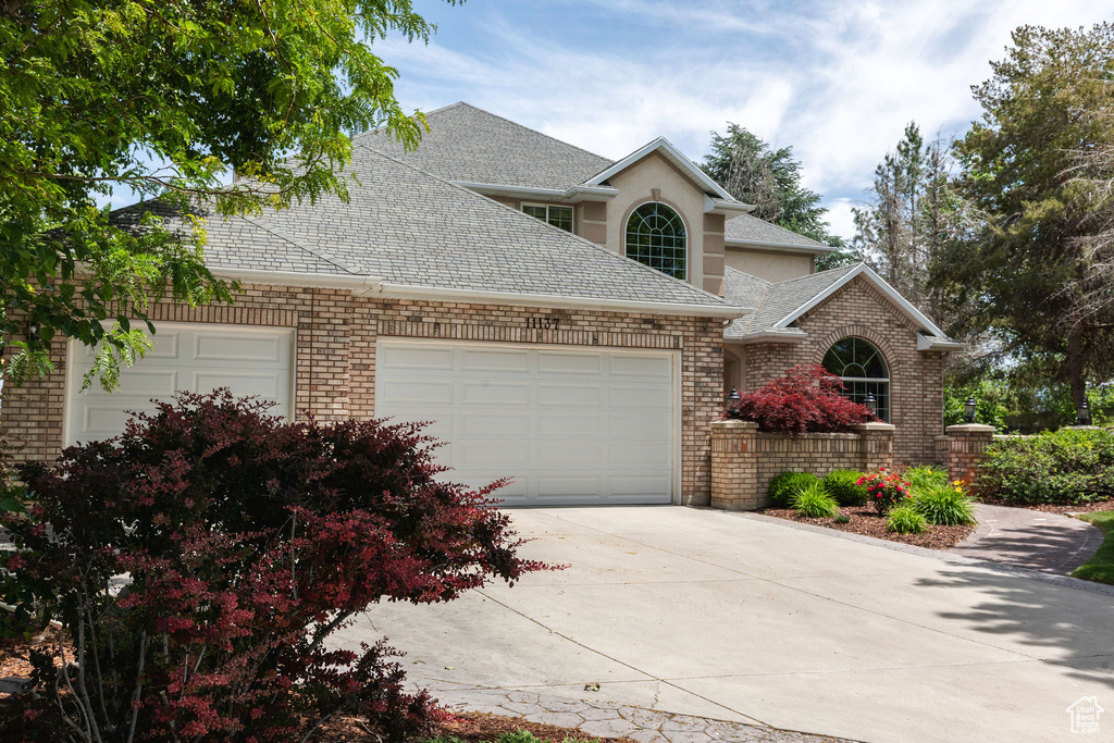 Traditional-style house with a garage, roof with shingles, concrete driveway, and brick siding