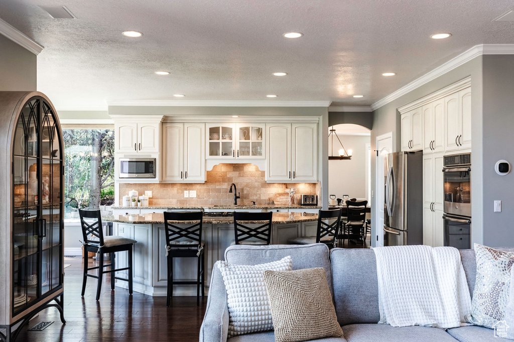 Kitchen with appliances with stainless steel finishes, a kitchen breakfast bar, light stone countertops, an island with sink, and decorative backsplash