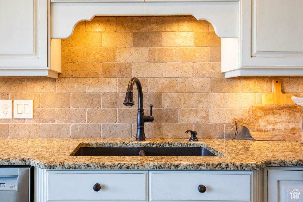 Kitchen view of light stone countertops, tasteful backsplash, white cabinetry, and dishwasher