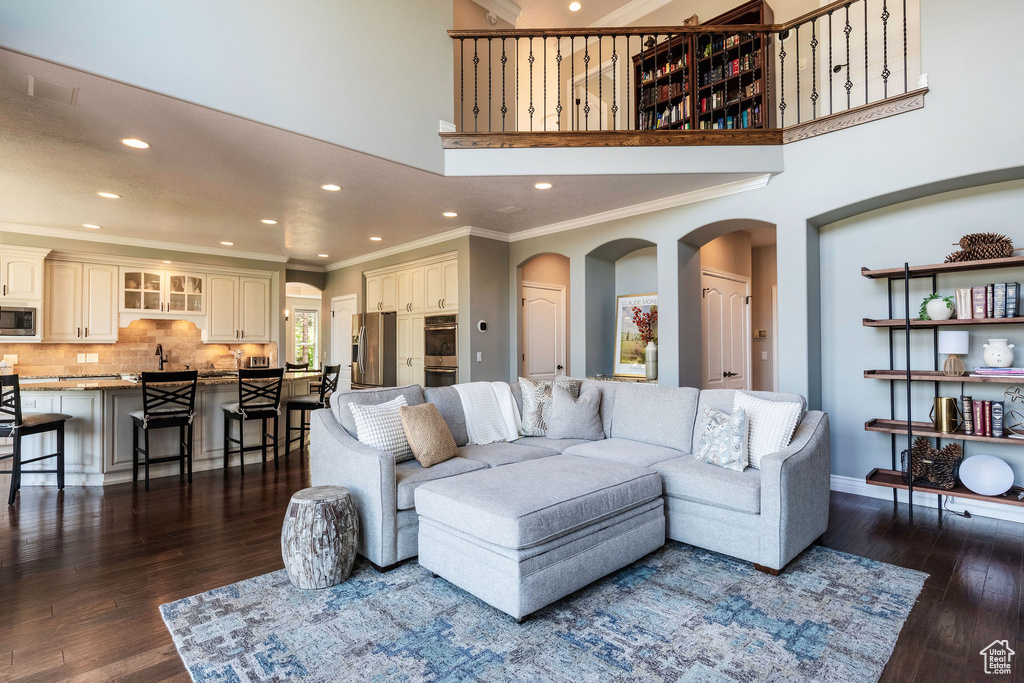 Living room with ornamental molding, recessed lighting, dark wood-style floors, arched walkways, and a high ceiling