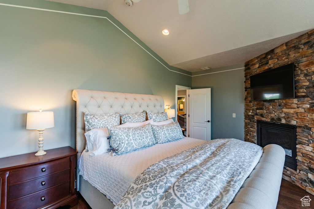 Bedroom with dark wood-style floors, lofted ceiling, a stone fireplace, and ceiling fan