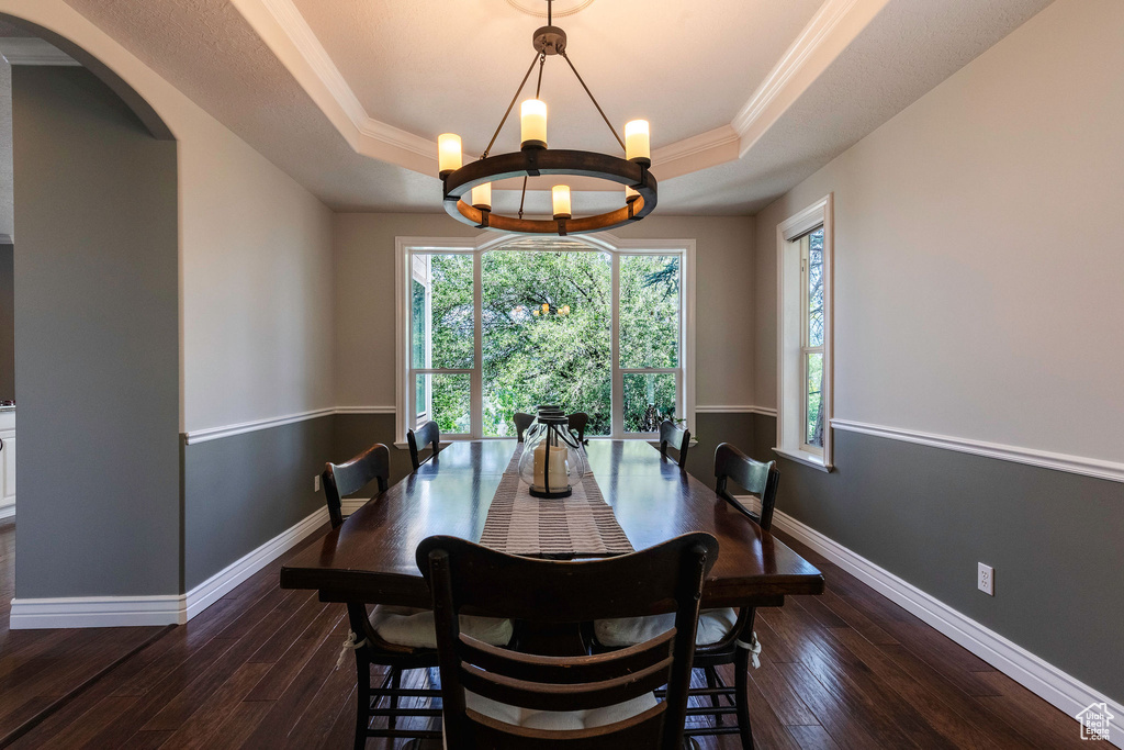 Dining space featuring a raised ceiling, hardwood / wood-style flooring, a chandelier, arched walkways, and crown molding
