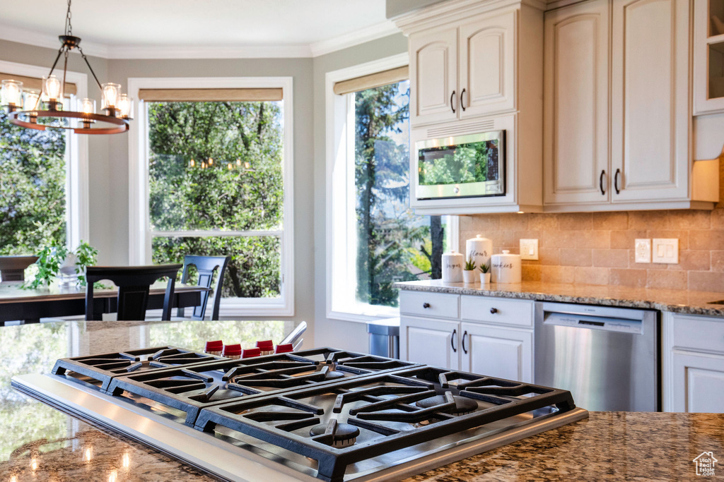 Kitchen with appliances with stainless steel finishes, a chandelier, decorative backsplash, light stone counters, and ornamental molding