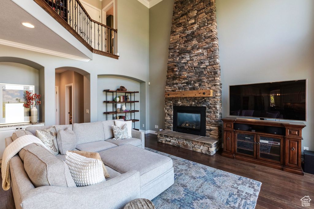 Living area with crown molding, arched walkways, a stone fireplace, dark wood finished floors, and a high ceiling