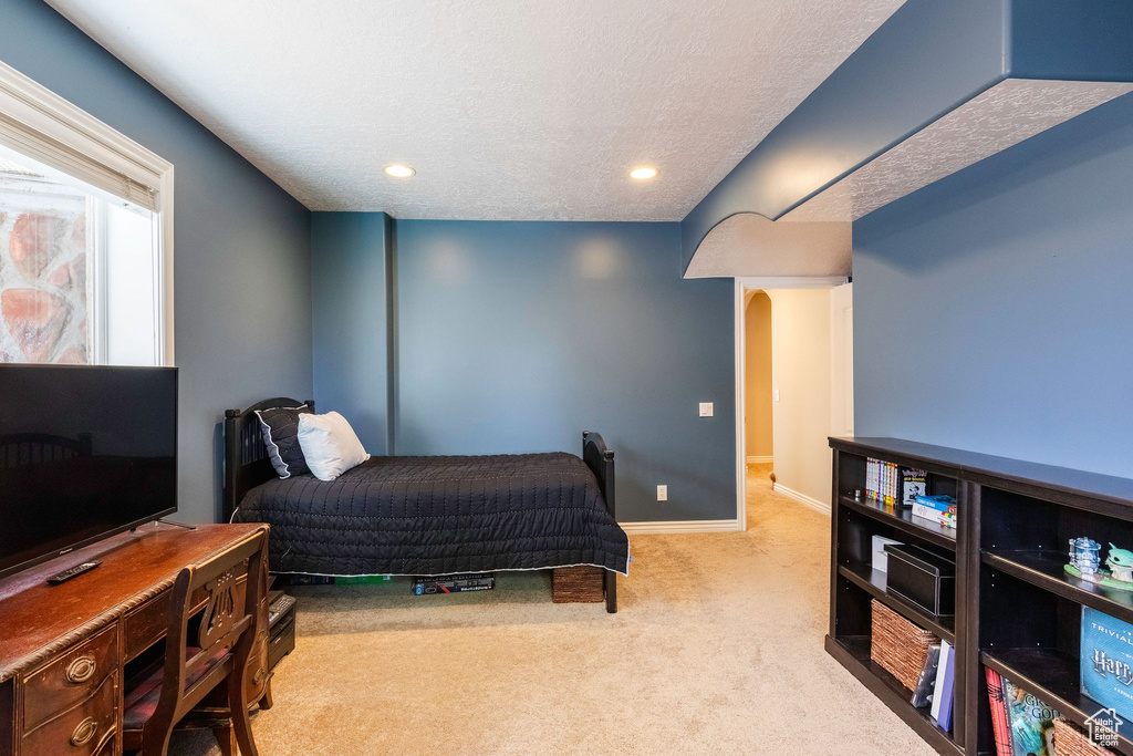 Carpeted bedroom with arched walkways, a textured ceiling, and recessed lighting