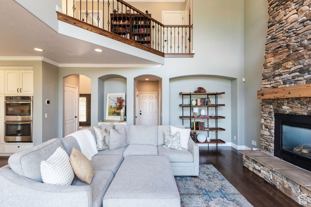 Living room featuring a stone fireplace, dark wood-style flooring, arched walkways, crown molding, and recessed lighting