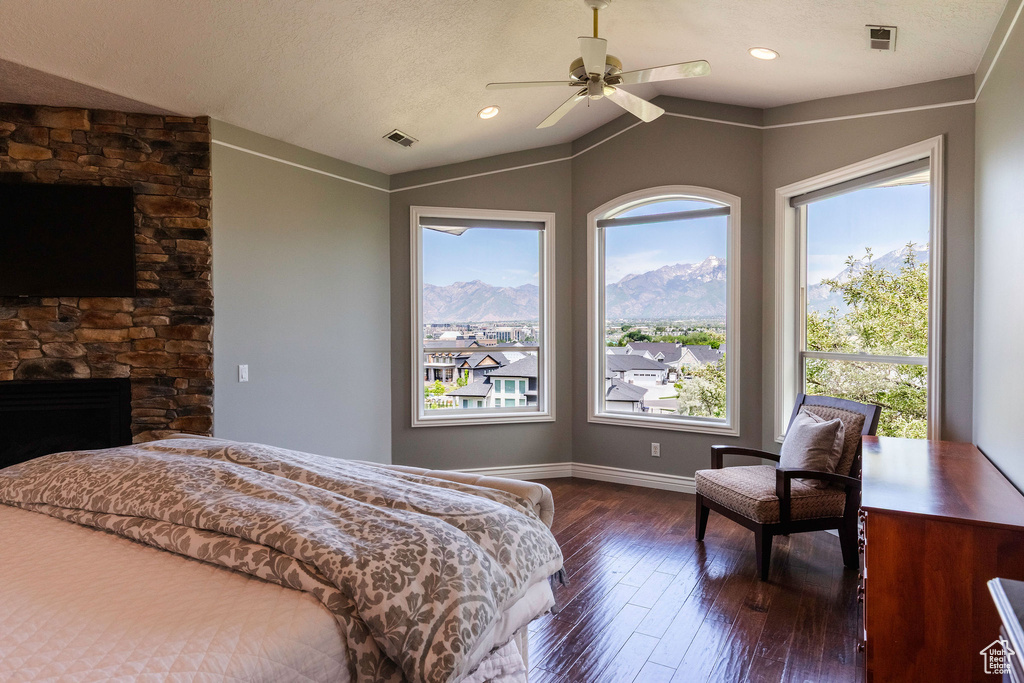 Bedroom with multiple windows, dark wood-style floors, vaulted ceiling, a fireplace, and a ceiling fan