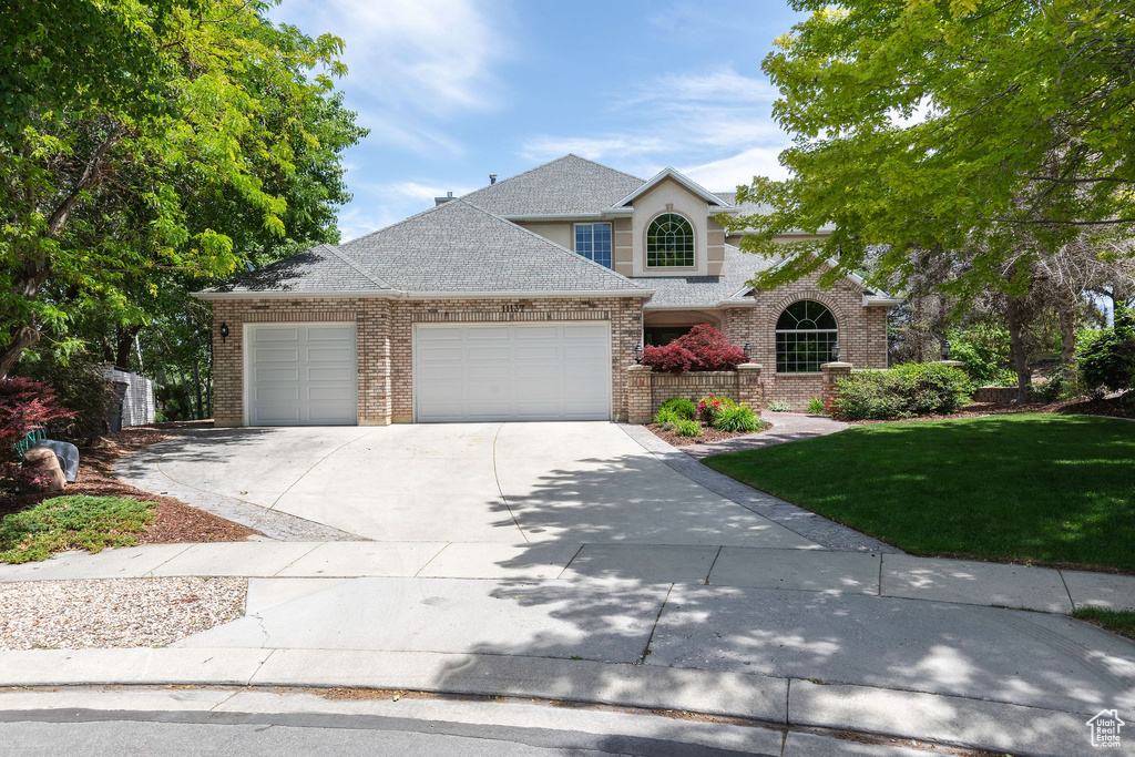 Traditional home with a garage, driveway, a front lawn, and brick siding