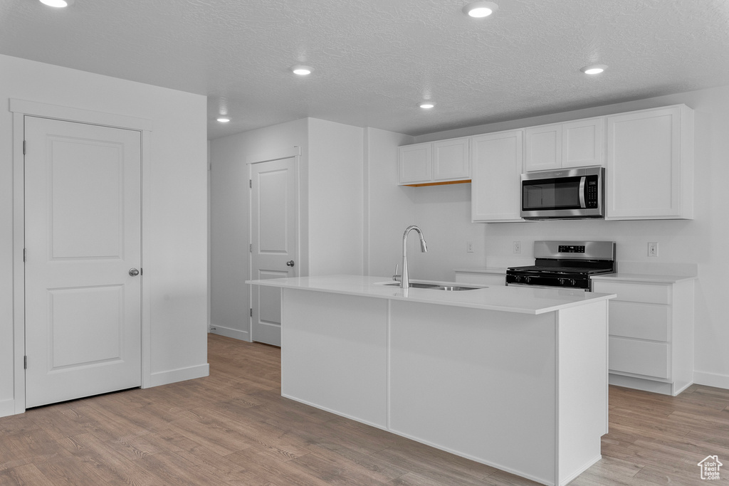 Kitchen featuring a sink, light countertops, appliances with stainless steel finishes, light wood finished floors, and white cabinetry