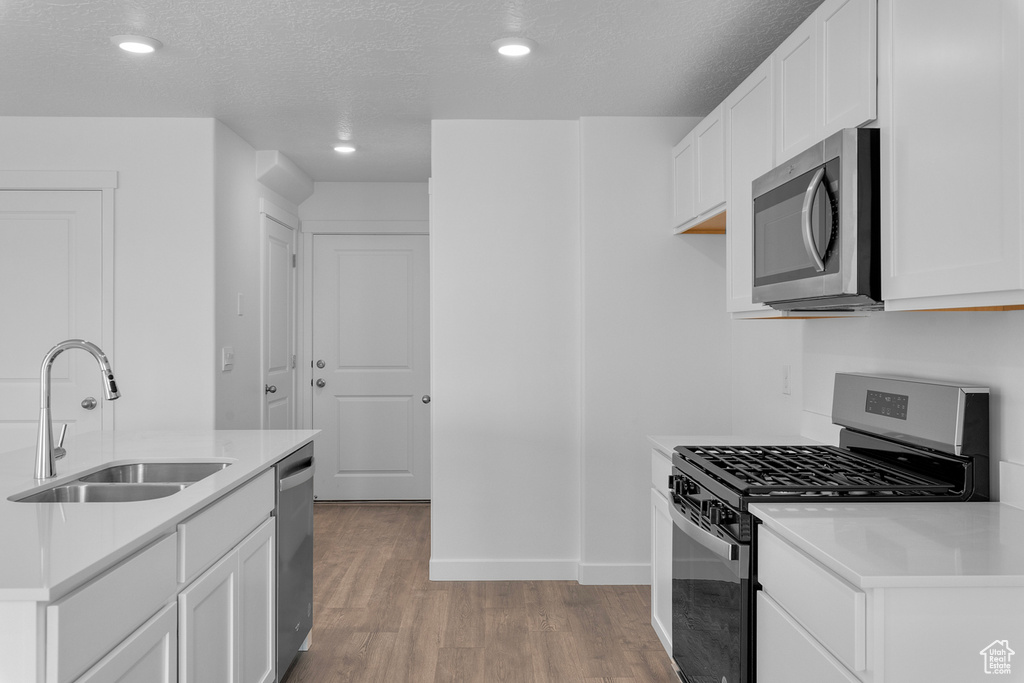 Kitchen featuring a textured ceiling, a sink, light wood-type flooring, recessed lighting, and appliances with stainless steel finishes