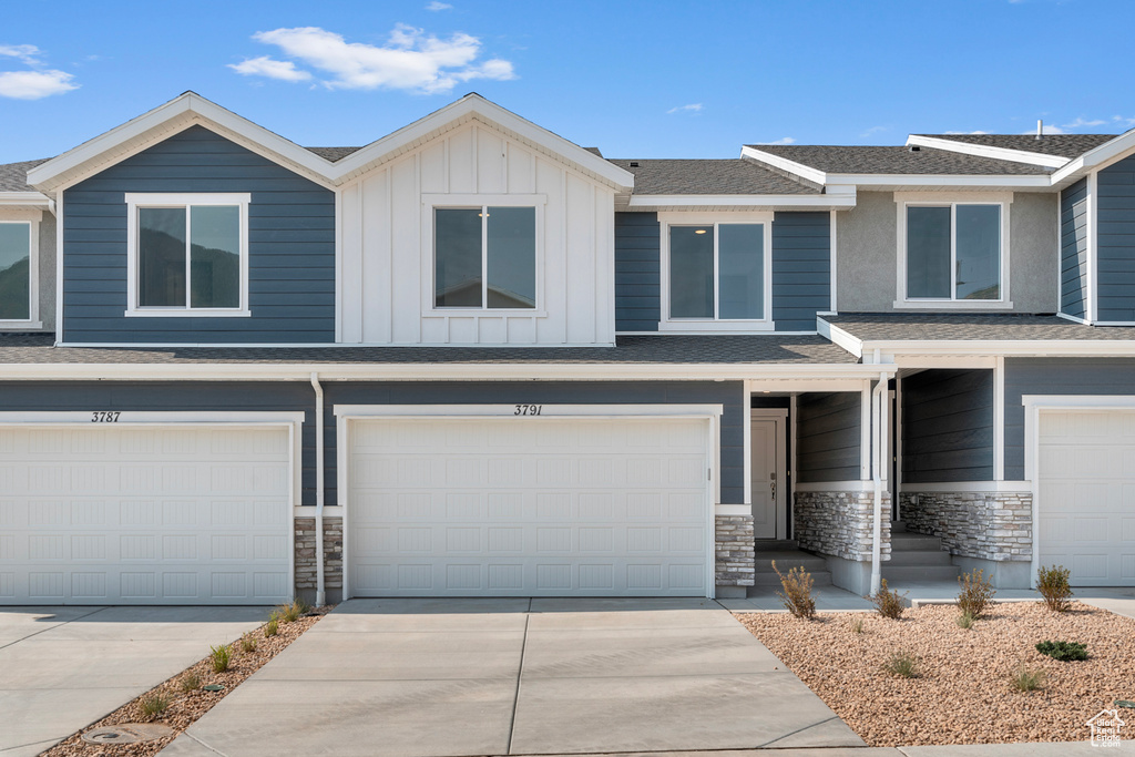 View of front of property with board and batten siding, an attached garage, stone siding, and concrete driveway