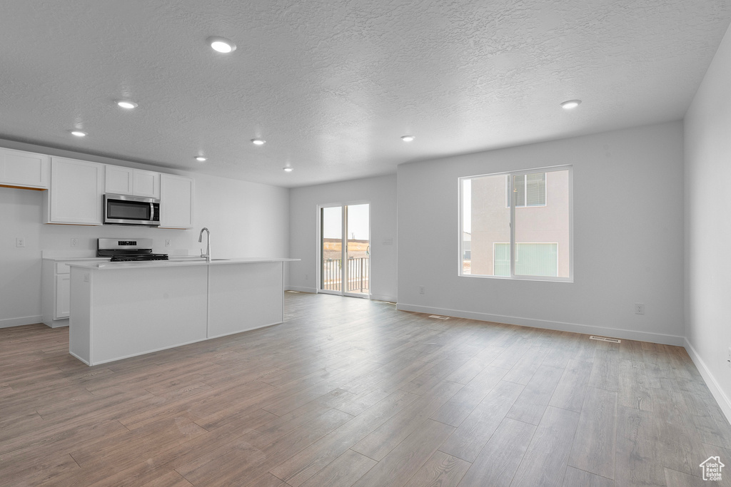 Unfurnished living room featuring recessed lighting, a sink, light wood-type flooring, baseboards, and a textured ceiling