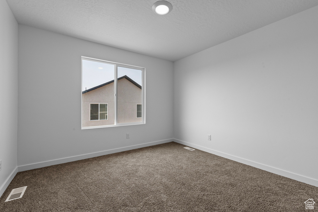 Carpeted empty room with baseboards, a textured ceiling, and visible vents