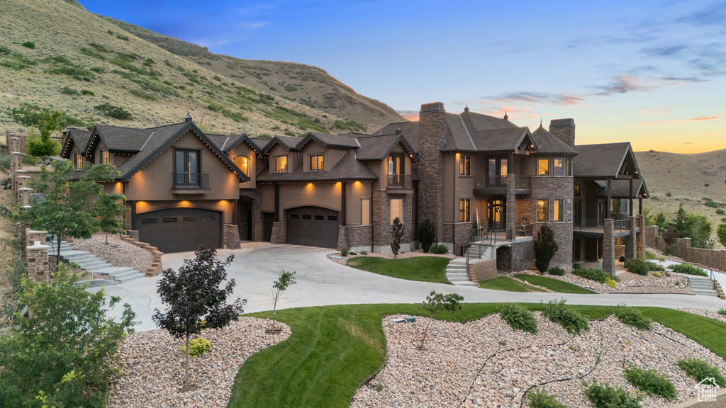 View of front of property featuring a balcony, stone siding, stucco siding, a chimney, and an attached garage