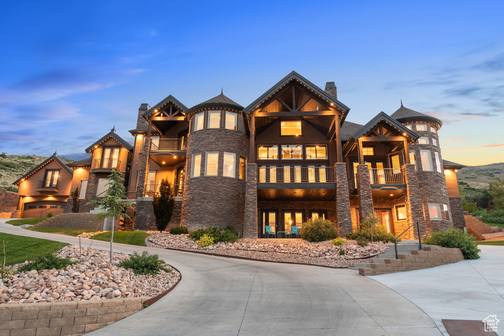 View of front of home with a balcony, stone siding, and a chimney