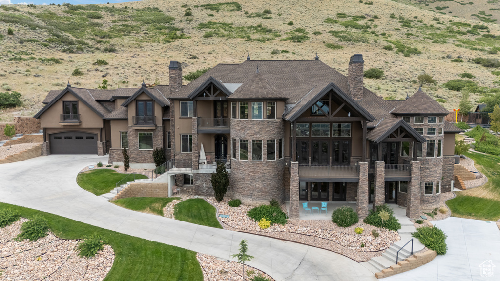 View of front of property featuring a balcony, stone siding, a chimney, and stucco siding