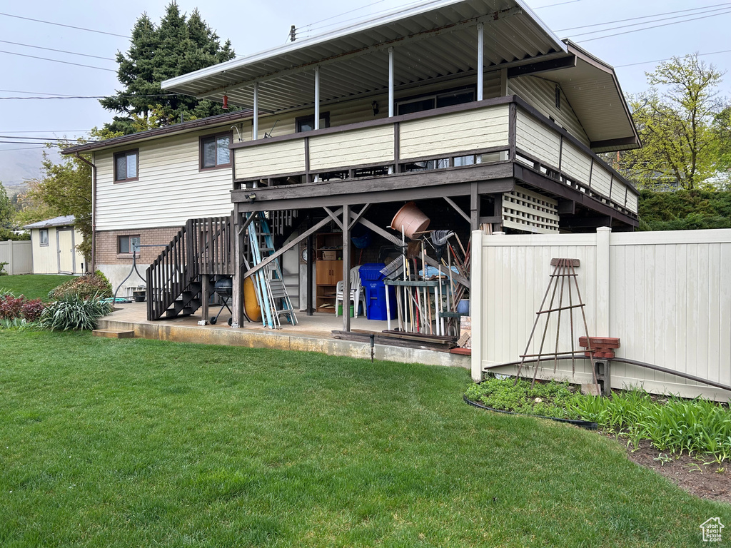 Rear view of house with stairs, fence, a wooden deck, a patio, and a lawn