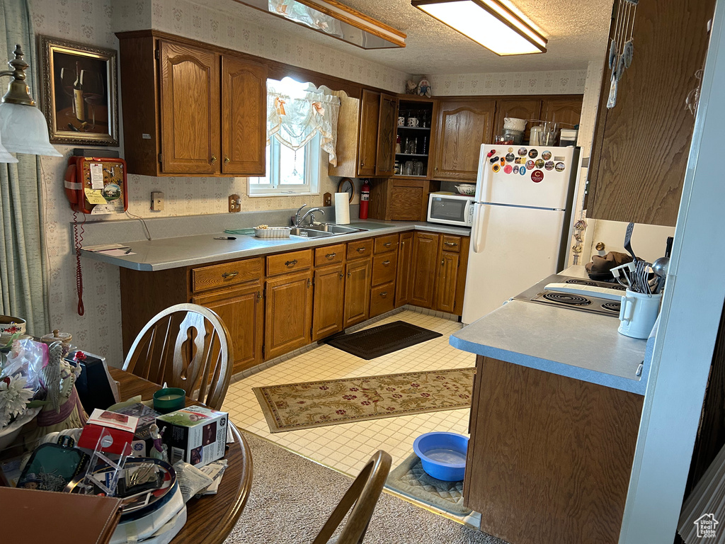 Kitchen featuring wallpapered walls, light countertops, a sink, white appliances, and brown cabinetry