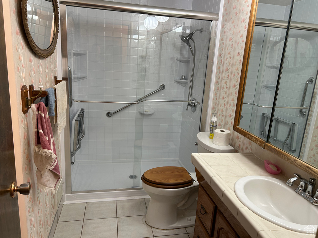 Bathroom featuring wallpapered walls, toilet, a shower stall, and tile patterned floors