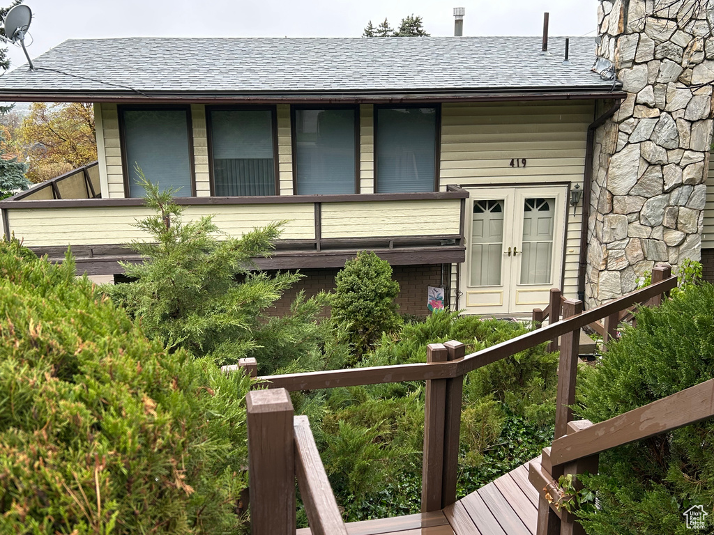 View of front of house with french doors, a shingled roof, stone siding, and a balcony