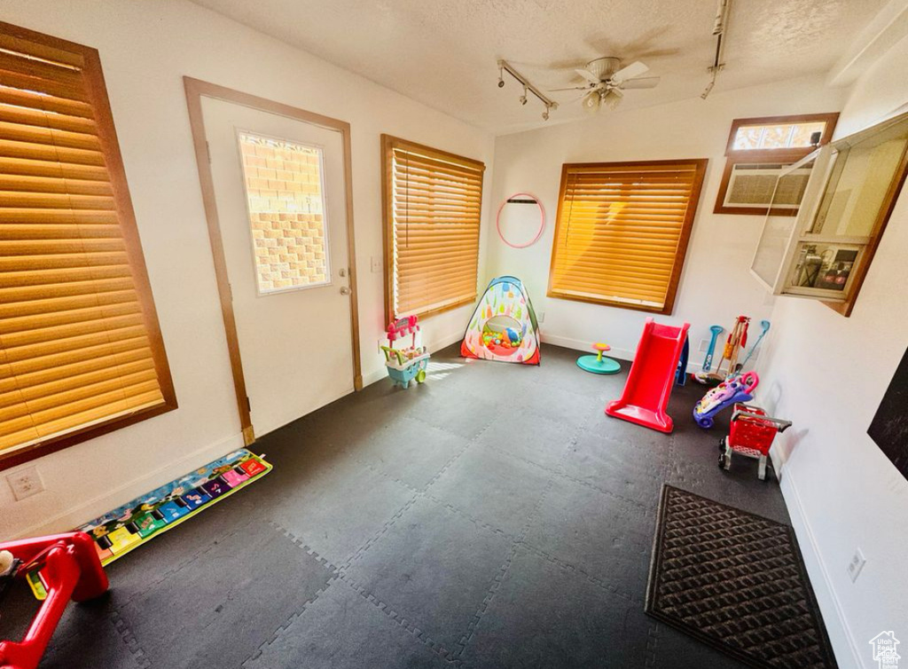 Rec room with rubber floors, rail lighting, baseboards, ceiling fan, and a textured ceiling