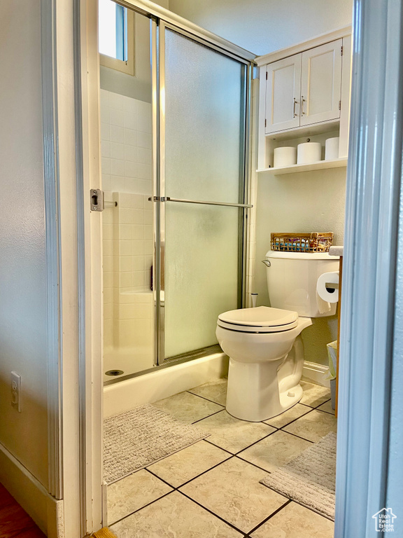 Bathroom with toilet, a shower stall, tile patterned flooring, and baseboards