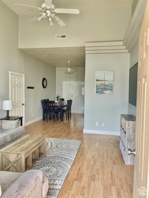Living area featuring ceiling fan, a high ceiling, light wood-type flooring, and baseboards