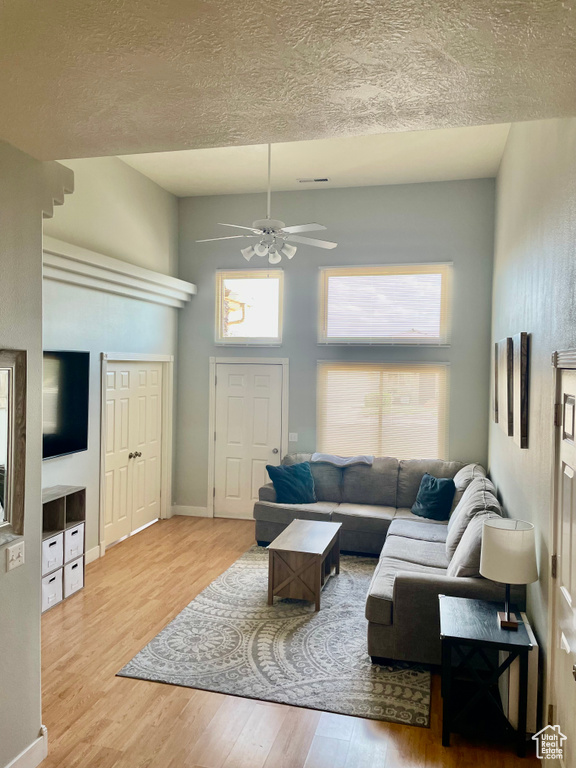 Living room featuring wood finished floors, a ceiling fan, a high ceiling, a textured ceiling, and baseboards