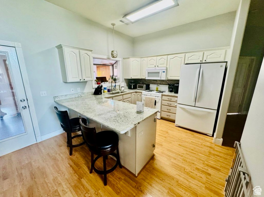 Kitchen featuring white appliances, a peninsula, a sink, a breakfast bar, and white cabinets
