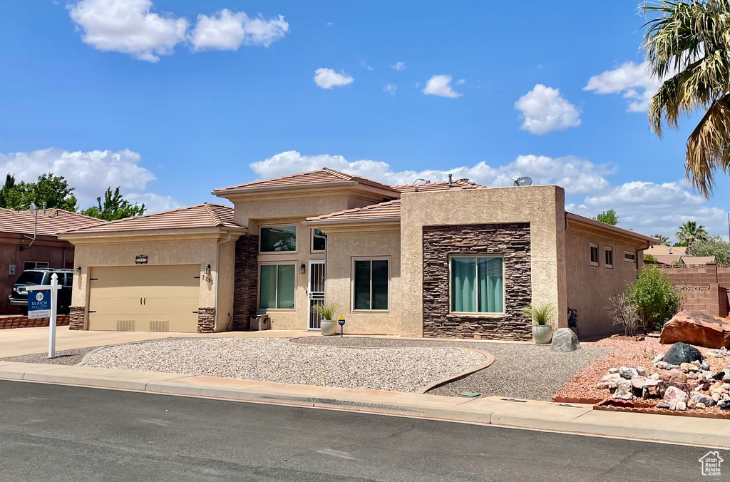 View of front facade featuring stone siding, stucco siding, an attached garage, a tiled roof, and concrete driveway