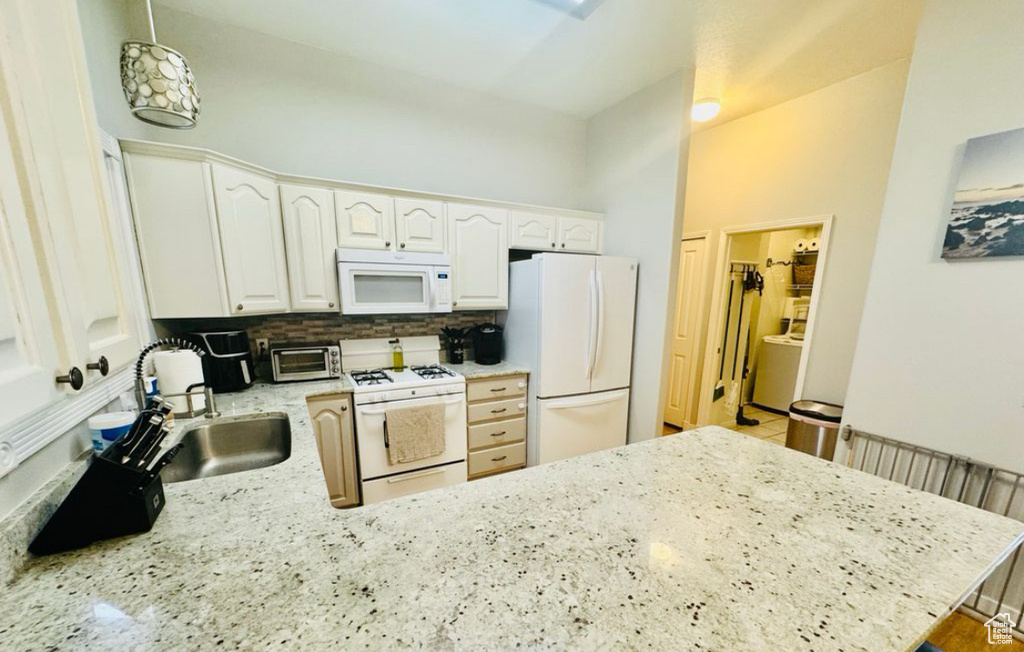 Kitchen with white appliances, a sink, a peninsula, light stone counters, and white cabinetry